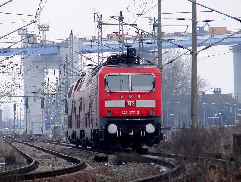 143 277-2 schiebt den RE33209 nach Sassnitz. Im Dunst ist der Bahnhof Stralsund - Rgendamm zu erkennen(h.rechts).  (am 05.03.06) 