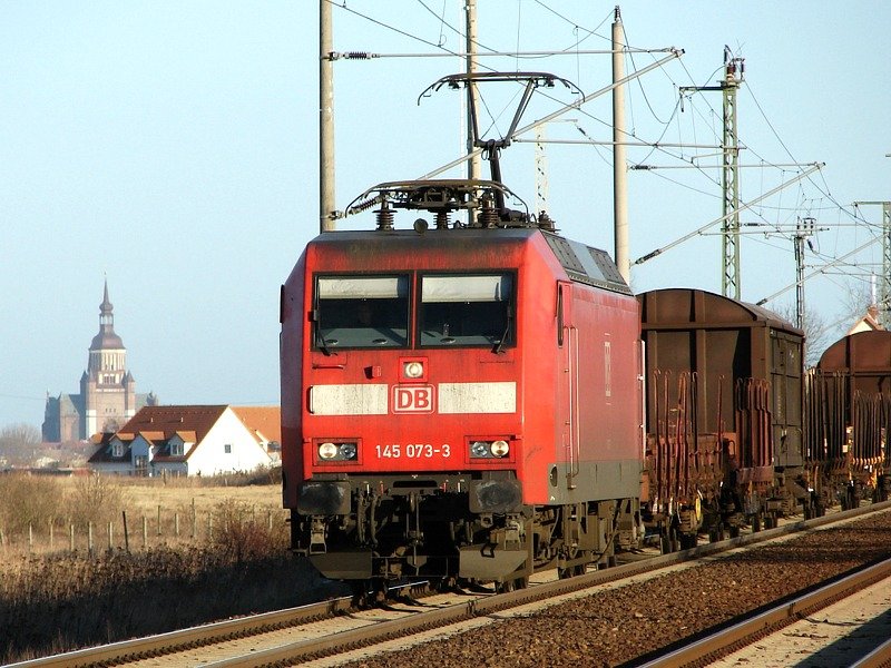 145 073 bei der Durchfahrt durch Stralsund-Langendorf. Im Hintergrund ist die Marienkirche in Stralsund zu sehen. (03.02.07)