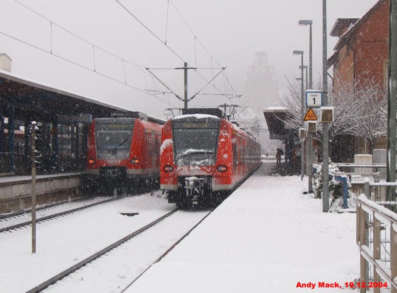 19.12.2004: Ein RE, bestehend aus zwei ET 425, verlsst den Bahnhof Herrenberg in Richtung Stuttgart, whrend auf Gleis 2 die S1 nach Plochingen auf ihre Abfahrt 6 min spter wartet. Das Schneetreiben hat die Zge, den Bahnhof und die Stadt in eine Winterlandschaft verwandelt und so tritt die Stiftskirche am Schloberg nur schemenhaft hervor...
