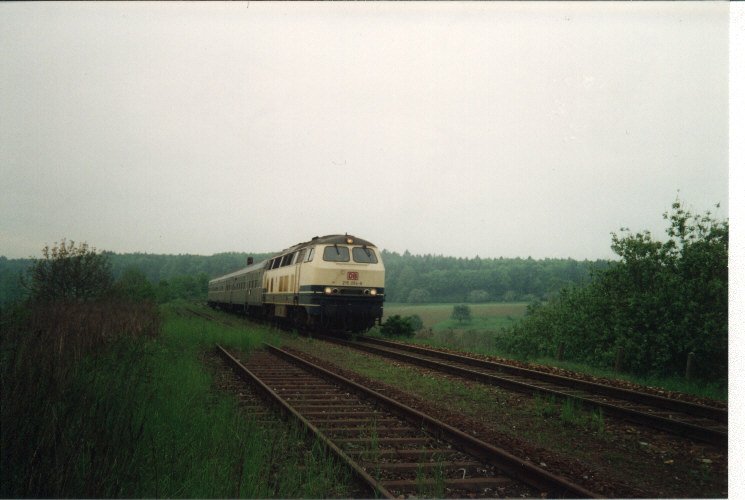 215 054-8 beim Einfahren in den kleinen Bahnhof Bauerbach (Stadtteil von Bretten). Das Bild muss um 1996 entstanden sein. Damals waren die 215er planmig Vormittags mit den Nahverkehrszgen auf der Kraichgaubahn unterwegs. Die Eilzge bernahm die Baureihe 218. Seit 1997 ist dieses Bild nicht mehr mglich. Seitdem ist die Kraichgaubahn elektrifiziert und moderne S-Bahnen bestimmen hier den Alltag.