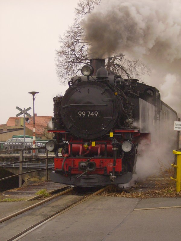 99 749 der Schs.-Oberlausitz-Eisenbahn zuckelt mit ihrem Regelzug am Mittag des 23.12.2006 von Zittau durch die gleichnamige Stadt in Richtung Bertsdorf.
Die Konstruktion im Hintergrund drfte wohl ziemlich einmalig sein: Bahnbergang auf einer alten Stahlbrcke.