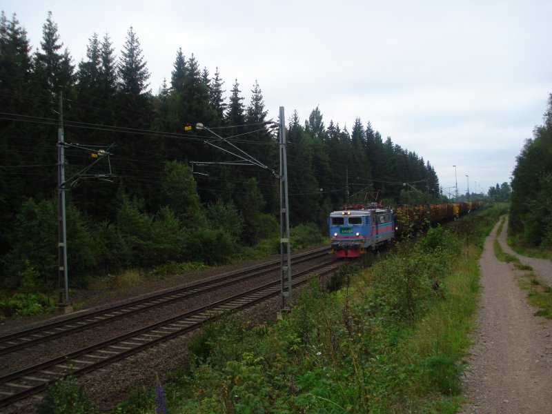 Am 21.08.2007 befhrt eine Rc1 vor einem mit Baumstmmen beladenen Gterzug die Sdra Stambanan.