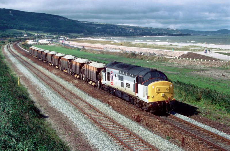 Am 26. August 1996 fahrt 37413 entlang der walisische Kueste mit einem Schotterzug aus Penmaenmawr.
