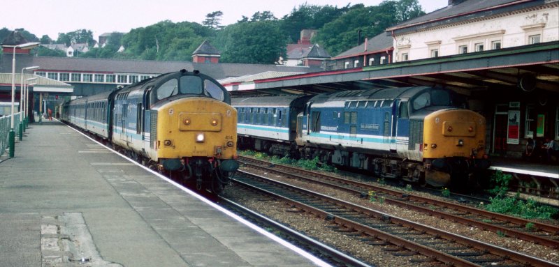 Am 5. September 1996 warten 37414 (links) und 37418 (rechts) in Bangor auf Weiterfahrt nach Crewe. Die Lokomotiven und Wagons tragen die Farben von der Regional Railways, einem Geschaeftsbereich von British Rail.