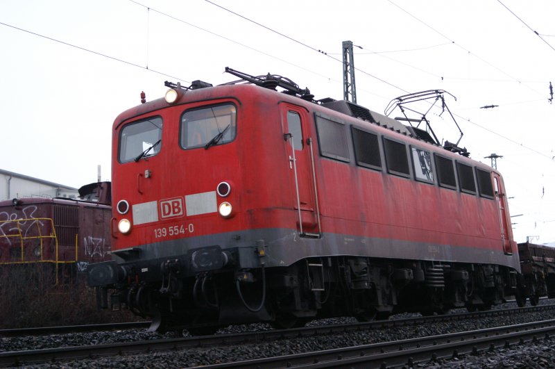 Am uerst trben  verschneeregneten  13.02.2009 zieht 139 554-0 einen lngeren Zug unbeladener Niederbordwagen am Lokschuppen des Rangierbahnhofs Hagen-Vorhalle vorbei, nachdem sie, bis vor wenigen Sekunden, ca. 20min lang vor einem Signal gewartet hat.