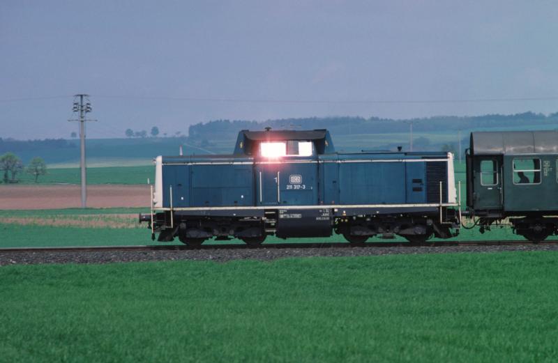 Am spten Nachmittag des 5. Mai 1989 ist 211 317-3 mit Ihrem Nahverkehrszug aus Umbauwagen von Coburg nach (damals noch nicht Bad) Rodach unterwegs, als sich die Sonne zwischen Meeder und Kleinwalbur in Ihrer Seitenscheibe reflektiert. Aufnahme: Contax 167 MT, Carl-Zeiss-Sonnar 1:2,8/135 mm; Film: Fuji RD 200 (CT)