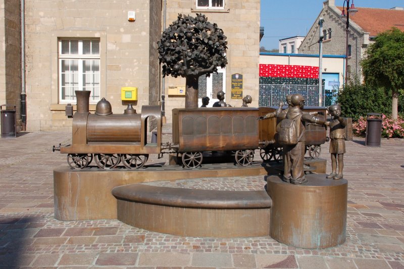 Auf dem Bahnhofsvorplatz von Diekirch (im Nordosten Luxemburgs gelegen) ist diese Skulptur einer Eisenbahn mit darum herum spielenden Kindern aufgestellt. Der Bahnhof Diekirch liegt als Endbahnhof an der Stichstrecke Ettelbrck - Diekirch und verbindet den Ort mit dem Hauptbahnhof Luxemburg. Regelmig angefahren wird der Bahnhof von Triebzgen der Reihe 2000.