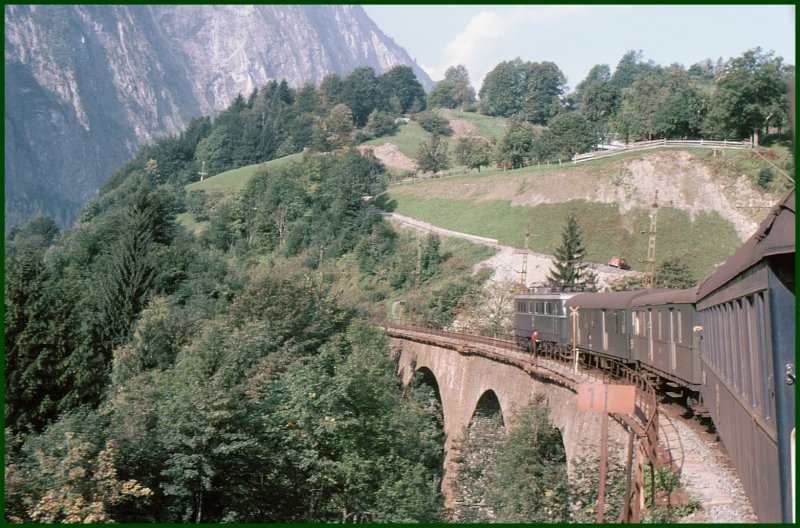 Auf der Rckfahrt in die Schweiz berqueren wir eine der zahlreichen Brcken auf der Arlberg-Westrampe. Interessanterweise steht auf der Brcke neben der Lok ein Mensch, was der dort zu suchen hatte, weiss ich auch nicht. (Archiv 09/75)
Lok vermutlich eine 1110 in grn.