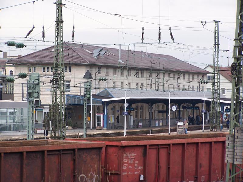 Bahnhof Aalen: Blick auf das Bahnhofsgebude mit an Gleis 1 wartenden Fahrgsten in Richtung Stuttgart. Links ist ein Teil des seit 2002 bestehenden Fahrradparkhauses zu erkennen. Im Vordergrund wird gerade eine leere Garnitur offener Gterwagen rangiert.