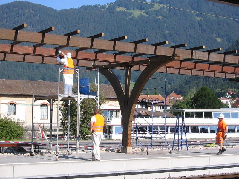 Bahnhof Interlaken West im Juli 2003. Eine der Bahnsteig-berdachungen wurde gerade erneuert. Ganz im Hintergrund kann man die oberen Deckaufbauten eines der Schiffe sehen, die unter der Regie der BLS den Thuner See befahren; der kleine Hafen liegt direkt hinter dem Bahnhof.