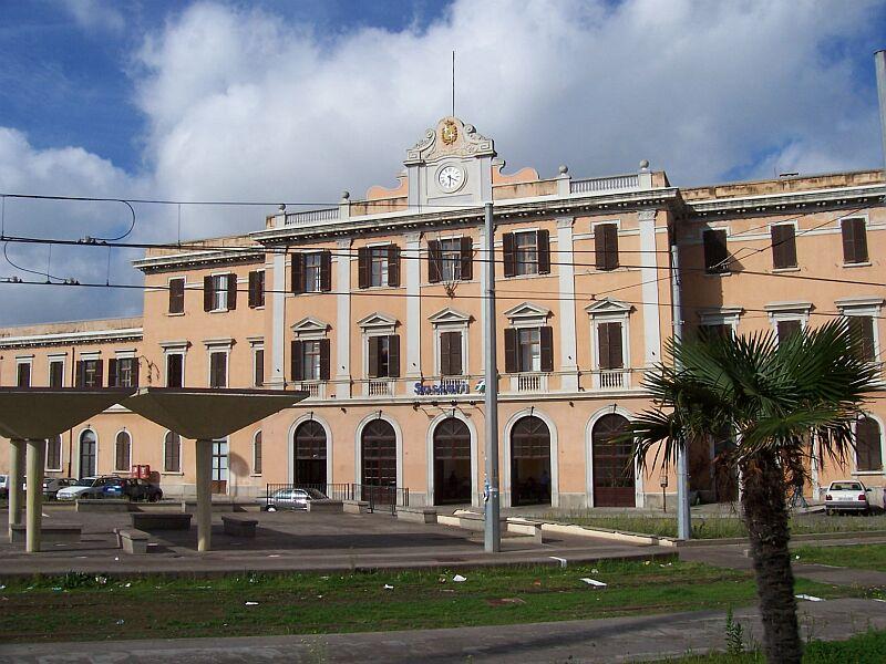 Bahnhof Sassari von der Straenseite am 20.10.2005, davor eine neue Meterspur-Haltestelle mit  Betonpilzen , neu elektrifiziert, aber alte Gleise, die mit denen im Bahnhof verbunden sind. Hier wird anscheinend eine Strecke reaktiviert, die erste Elektrische auf Sardinien.