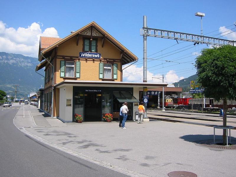 Bahnhof Wilderswil im Juli 2003. Der Bahnhof liegt an der Strecke der Berner Oberland Bahn (BOB) zwischen Interlaken Ost und Grindelwald bzw. Lauterbrunnen. Auerdem besteht hier eine Umsteigemglichkeit zu den Zgen der Schynige-Platte-Bahn, deren Depot im Hintergrund zu erkennen ist.