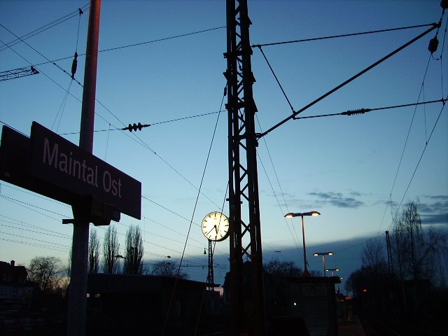 Bahnofs Uhr, Oberleitung und Bahnhofs Schild in Maintal Ost.