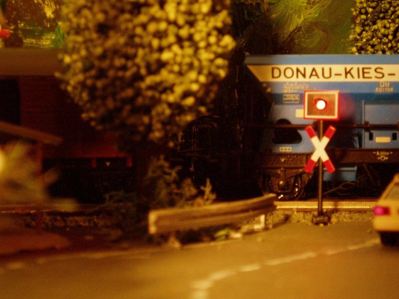 Bei Abendrot passiert ein Gterzug den Bahnbergang am  stlichen , hinteren Anlagenbereich.