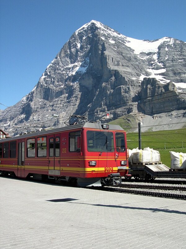 Berner Oberland 2007 - Mit einer Ladung asiatischer Fahrgste kommt am 26.07.2007 der Triebwagen 212 der Jungfraubahnen vom gleichnamigen Berg und der noch dazu hchsten Bahnstation Europas. Im Hintergrund ist der Eiger mit seiner faszinierenden Nordwand zu sehen. Unterhalb der Nordwand befindet sich der sogenannte  Eigertrail , der  hautnah  unter der Nordwand vom Eigergletscher nach Alpiglen fhrt. Selbstverstndlich lsst sich dieser Wanderweg auch in der Gegenrichtung benutzen - aber nur bei guter Kondition! Die Jungfraubahn fhrt brigens mit dem seltenen Stromsystem 1125V Drehstrom und benutzt als einzige Bergbahn im Berner Oberland das Zahnradsystem Strub.