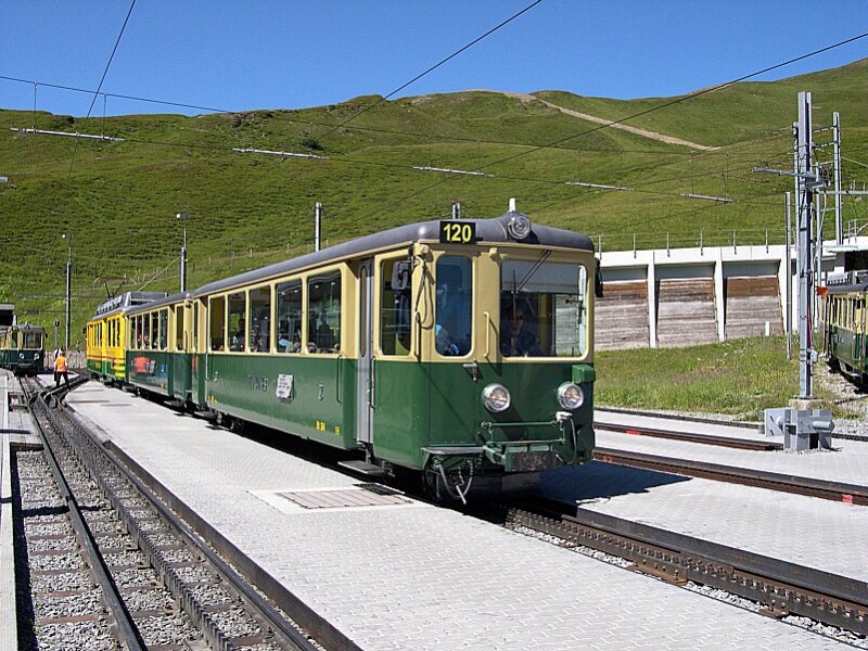 Berner Oberland 2007 - Mit unserem Zug auf der Kleinen Scheidegg angekommen, suchen wir uns erstmal einen freien Platz um uns etwas mit Creme vor der Sonne zu schtzen. An diesem tag ein etwas schwieriges Unterfangen. Zwischenzeitlich macht sich BDt 120 der WAB wieder startklar fr die Rckfahrt nach Lauterbrunnen. Der Holzbau im Hintergrund rechts neben dem Fahrzeug gehrt brigens zum 120m langem Kleine Scheidegg-Tunnel. Dieser besitzt je einen Ausgang Richtung Lauterbrunnen und Grindelwald und ist als Spitzkehre angelegt. So kann man Zge aus Grindelwald drehen und nach Lauterbrunnen fahren lassen. Grund ist das betrieblich das Triebfahrzeug bei Bergbahnen immer auf der Talseite stehen muss. 