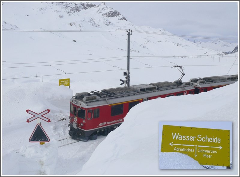 Berninaexpress 953 mit ABe 4/4 III 54  Hakone  an der Spitze passiert soeben den krzlich ausgegrabenen Bahnbergang zum Kieswerk am Lago Bianco. Dahinter steht die Wasserscheidetafel, zur besseren Lesbarkeit nochmals im Vordergrund abgebildet. Sinngemss schmilzt der linke Schneehaufen Richtung Adda und Po ins Mittelmeer und die Seite rechts der Strasse ber Inn und Donau ins Schwarze Meer. (10.03.2009)