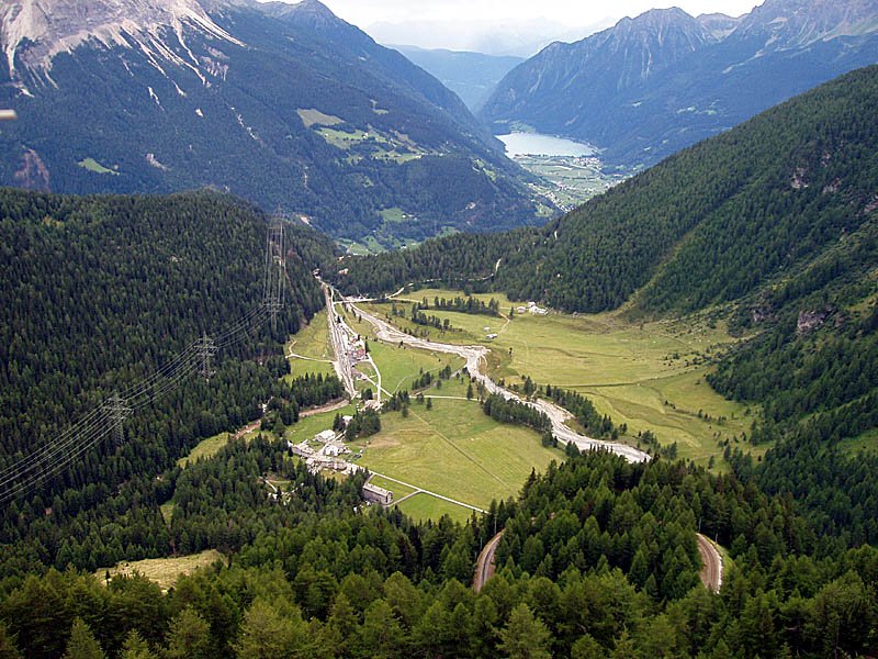 Blick von der Alp Grm in Richtung Lago di Poschiavo, Tirano. Bhf. Cavaglia (Mitte) und oberhalb liegende Kehre der Berninabahn (unten rechts) sichtbar, 06. Aug. 2006