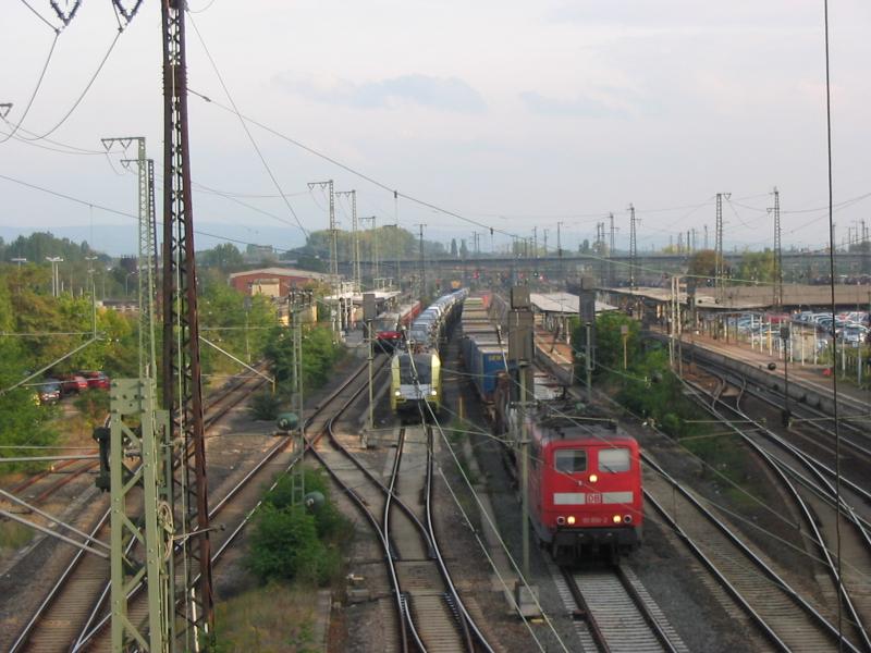 Blick ber das sdliche Gleisfeld des Hanauer Hauptbahnhofs im September 2004. Auf Gleis 2 steht ein Vollzug der S-Bahn-Linie S8 oder S9, bestehend aus zwei verkehrsroten 420ern, auf den Durchfahrtsgleisen 3 und 4 ein Dispo-Taurus und eine verkehrsrote 151 mit ihren Gterzgen, sie warten darauf, von einem ICE berholt zu werden.