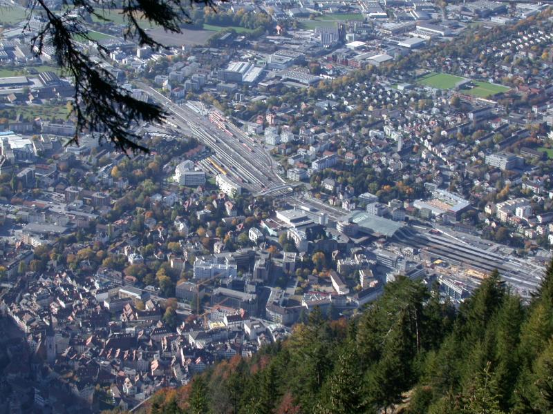 Chur Kantonshauptstadt Graubndens und Verkehrsknotenpunkt mit bergang von den SBB zur RhB und den vielen Postautolinien.
In Bildmitte unter dem Glasdach befindet sich die Postbusstation, rechts davon der Personenbahnhof und links davon die Abstellanlagen und Gterbahnhof. Die obere Hlfte bentzt die schmalspurige RhB, den untern Teil die SBB. Blick vom Mittenberg am 24.10.2004.