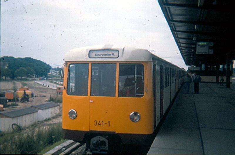 Dann gibt es jetzt endlich auch mal ein Foto der U-Bahn in  Hauptstadt-Lackierung . Hier eine Dora-Einheit mit der BVB (Ost) Nummer 341-1 am U-Bf. Elsterwerdaer Platz. Diese Zge wurden von der damaligen BVG (West) an die DDR abgegeben. Zum Ausgleich dazu sollte die damalige DDR-Regierung die Transit U-Bahnlinien 6 und 8 fr fnf Jahre unterhalten. Die Ereignisse berrollten die Sache jedoch denn nach 5 Jahren gab es keine DDR mehr. Die damalige Bahnindustrie der DDR baute unter Hochdruck Elektrolokomotiven und hatte keine Kapazitten fr die dringend bentigten Fahrzeuge zur Streckenverlngerung Richtung Hnow. Hier ist der Erffnungstag des Teilabschnitts zum Elterwerdaer Platz zu sehen. Wie in der DDR blich, war die gesamte Umgebung noch eine einzige Baustelle.