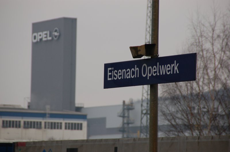 Das Schild vom Bahnhof Eisenach-Opelwerk. Im Hintergrund ist der Turm des Eisenacher Opelwerks zu sehen. 22.02.2007