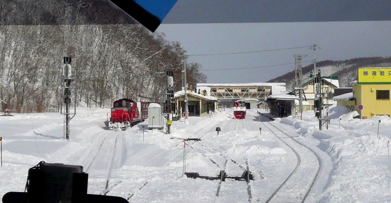 DD51 1086 steht im Bahnhof Engaru (Ost-Hokkaido) mit einem Containerzug bereit für die Fahrt über den Pass nach West-Hokkaido. Im Mittelgleis des Bahnhofs steht eine Schneefräse, auf dem Bahnsteigdach sieht man Bahnarbeiter, die den Schnee herabschaufeln. 17.Februar 2009. (Aufnahme durch die verglaste Führerstandsrückwand eines Panorama-Steuerwagens.) SEKIHOKU-HAUPTLINIE 