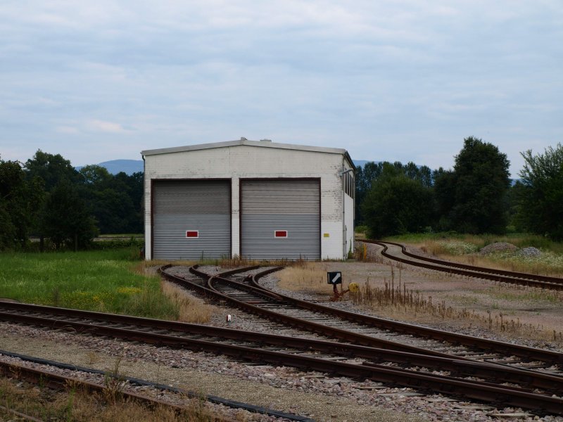 Der Lokschuppen der V100 der SWEG in Schwarzach. Der Lokschuppen befindet sich in Mitten des Gleisdreiecks Schwarzach. Man kann die drei Gleise ansatzweise im Hintergrund erkennen. Hinter dem rechten Tor parkt die V100. Fotografiert am 14. Juni 2008.