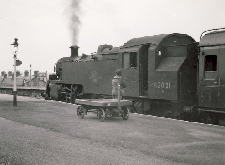 Die 82021 hat in Machynlleth den hinteren Teilzug des Cambrian Coast Express (London-Aberystwyth/Pwllheli) abgeholt und wartet nun damit in der Lokalbahnatmosphre von Towyn (Tywyn) auf die Abfahrt Richtung Pwllheli; 17.Juli 1964. Die Standard-Loks der Serie 82000 (82000-82044) wurden ab 1952 erbaut.