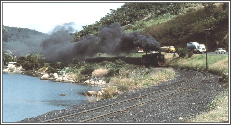 Die Dampflok mit ihrem langen Kohlenzug zum Hafen von Imbituba berholt hier bei Lagoa eine schleichende Autokolonne auf der parallelen BR 101.(Archiv 04/1981)