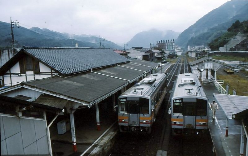 Die KIHA 120 des westjapanischen Hochlandes. Links wartet der KIHA 120-338 auf den Abfahrtsbefehl, rechts ist der KIHA 120-328 soeben angekommen; sein Wagenführer, in schmucker weisser Sommeruniform, begibt sich zum vorderen Führerstand für die Rückfahrt. Tôjô, 30.September 2001.