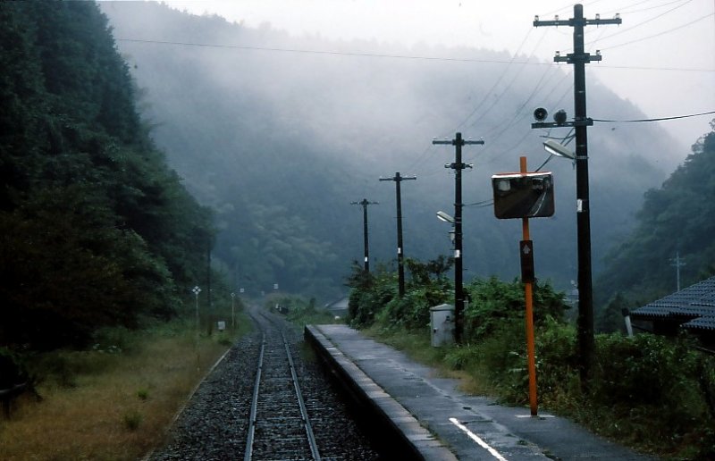 Die KIHA 120 des westjapanischen Hochlandes. Auf der Fahrt im KIHA 120-355 (im Spiegel knapp sichtbar) ist die düstere, nasse Haltestelle Tomihara erreicht. An vielen Stellen ragen die regennassen Büsche weit ins Lichtraumprofil hinein. 30.September 2001. 