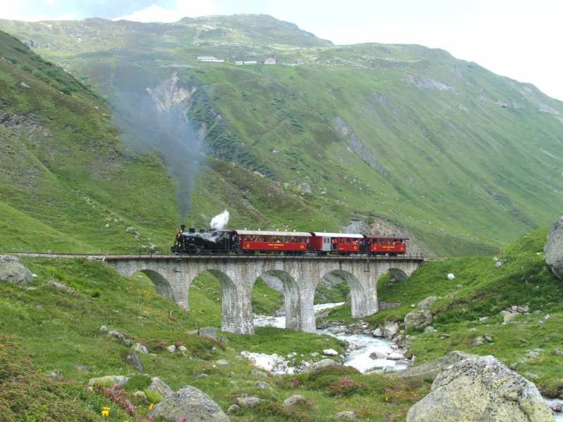 Die Lok HG 3/4 Nr. 4 mit rotem Zug berquert den Steinstafel-Viadukt (1900 mNN) der oberhalb Tiefenbach die Furka-Reuss berquert. Ganz oben im Bild ist der Weiler Tiefenbach an der Furka-Passstrasse zu erkennen.
23.06.2007
