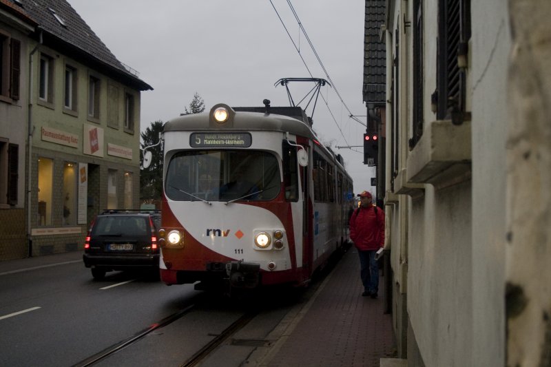 Die OEG bahnt sich ihren Weg im Autogegenverkehr durch Gro�sachsen. Sch�n finde ich hier, wie das Einfahrsignale f�r den Bahnhof Gro�sachsen an einer Hauswand befestigt ist.