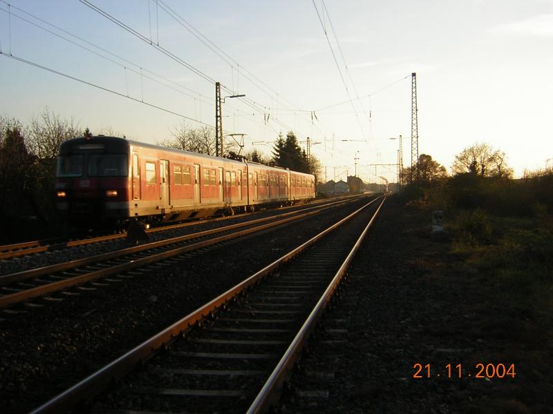 Die Sonne stand bereits sehr tief, als 420 317 auf der Linie S 7 am 21.11.2004 den im Hintergrund liegenden Bahnhof Mrfelden in Richtung Frankfurt am Main verlie.