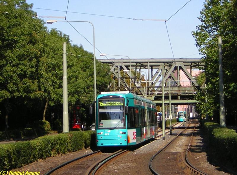 Die Straenbahntrasse kreuzt zwischen den Haltestellen Universittsklinikum und Heinrich-Hoffmann-Strae / 
Blutspendedienst die Strecke der Main-Neckar-Bahn unter
der analog dazu benannten Main-Neckar-Brcke. Auf der
Aufnahme vom 28.08.2005 hatte der 6. Zug der Linie 15 mit S-Triebwagen 207 zum Haardtwaldplatz die Brcke gerade 
hinter sich gelassen, im Hintergrund nherte sich der 
S-Triebwagen 215 auf dem 4. Zug der Linie 21 nach Schwanheim. 


