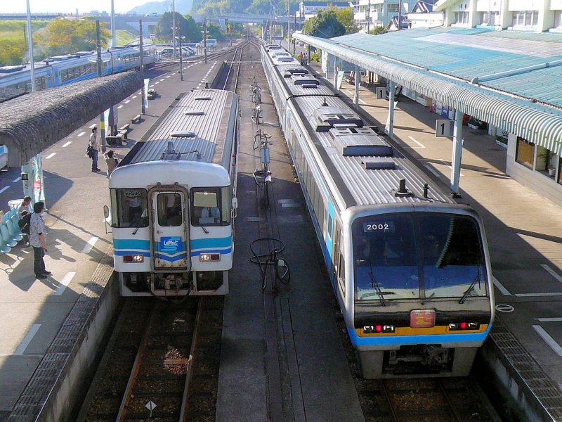 Die Tosa Kuroshio-Bahn (Westabschnitt): Tosa ist der alte Provinzname von Süd-Shikoku (heute Praefektur Kôchi), Kuroshio ist der Name der Meeresströmung, die östlich von Japan vorbeifliesst. Die Bahn will also das Gefühl einer Gegend mit alten Traditionen am offenen, weiten Meer an der (nur über hohe Pässe erreichbaren) Südseite der Insel Shikoku vermitteln. Der Lokalverkehr wird mit 8 Triebwagen Serie 8000 (im Bild links Nr.8005) gefahren, der durchgehende Intercity-Verkehr mit Verbindung bis nach Okayama auf der jap. Hauptinsel über die Grosse Seto-Brücke mit Zügen Serie 2000 (einer gehört der Tosa Kuroshio-Bahn, die anderen gehören JR Shikoku); hier ist der Zug mit Endwagen 2002. Nakamura, 20.September 2009. 