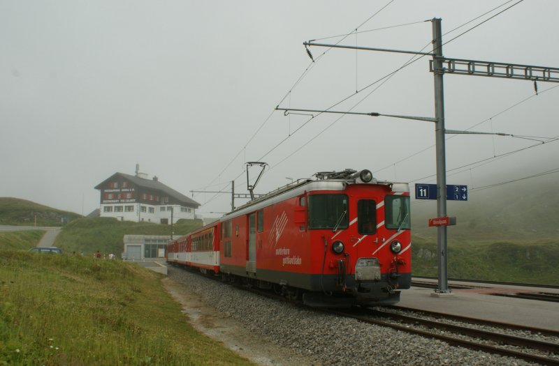 Drei Minuten nach der Aufnahme des Bildes ID 327 824 hat sich der Nebel ziemlich verzogen und das gemachte Bild lsst nun Details erkennen: Der Regio nach Disentis ist abgefahren, im Hintergrund verkndet das Restaurant Piz Clamot, dass wir uns auf 2048 mM befinden und der Regionalzug nach Andermatt, nun in seiner ganzen Lnge zu sehen, wartet auf die Abfahrt. 
22. August 2009