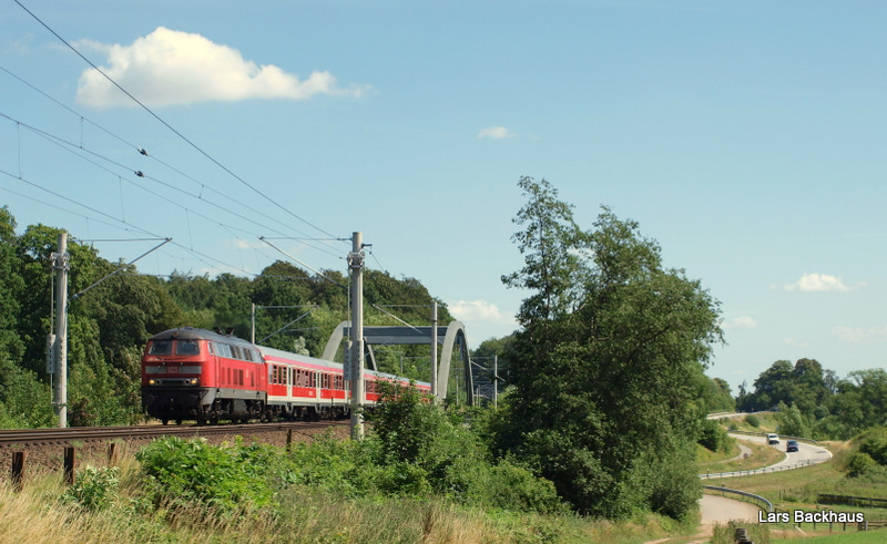 Durch das mit 218ern bespannte RE-Paar Hamburg - Lbeck - Kiel legt eine alte ra auf der Kbs 104 weiter. 218 104-8 dieselt am 16.07.09 mit dem RE 21417 ber die B75-Querung bei dem Ort Kneeden Richtung Bad Oldesloe. Rechts ist dann eine S-Kurve der B 75 zusehen.