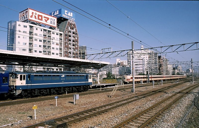 EF65 Serie 1000,die Standard-Universallok für flache Gleichstromstrecken. 3 zweiachsige Triebdrehgestelle. Insgesamt 139 Loks (Nr.1001-1139),Baujahre 1969-1972 und 1976-1979.Der Abbruch hat im November 2007 begonnen. Hier wartet die EF65 1124 mit einem Schlafwagenzug aus Kyushu mit Ziel Tokyo, während ein Pendolino-Intercity gerade einfährt. Shin Osaka, 14.März 1999.  