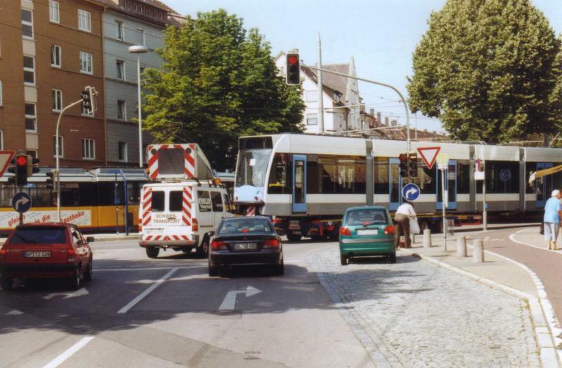 Ein funkelnagelneuer Triebwagen  Siemens Combino  f�r die Ulmer Stra�enbahn wird gerade per Spezialtransporter angeliefert. Das Bild entstand am Dienstag, 22. Juli 2003, in Ulm, amWestplatz, in unmittelbarer N�he des Stra�enbahnbetriebshofes der Stadtwerke Ulm. Im Hintergrund auf den Schienen ein alter  GT 4 -Triebwagen.