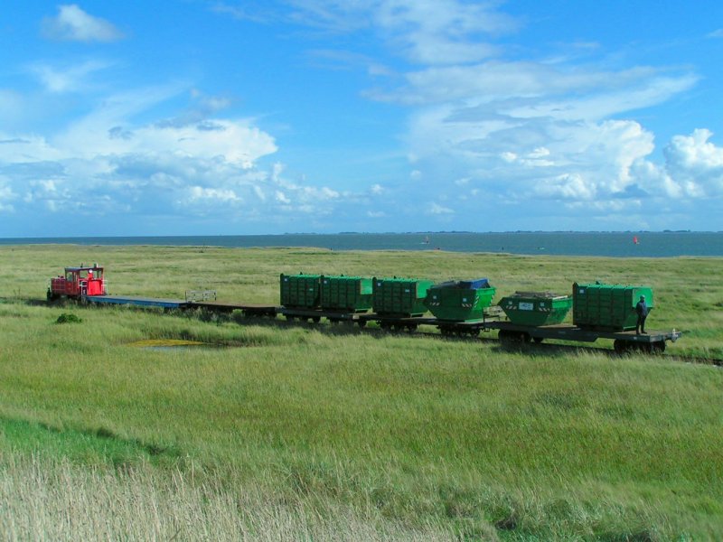 Ein Mllzug wird durch die Salzwiesen zum Hafen geschoben; 
Die beladenen Container werden dann mittels Gabelstapler auf die Fhre umgeladen und ins Festland zur Entsorgung transportiert.