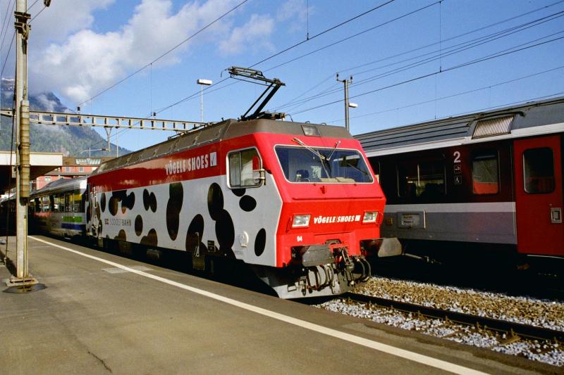 Eine HGE 4/4 mit der Werbeaufschrift  Vgele  zieht einen            Voralpen-Express. Arth-Goldau