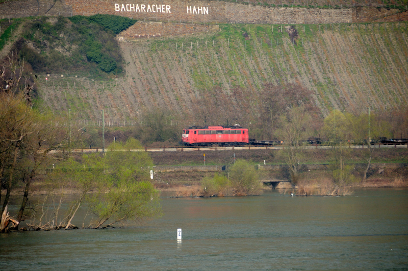 Eine unbekannte 140 zieht einen leeren Stahlbrahmen-Wagenzug unterhalb des  Bacharacher Hahns  die linke Rheinstrecke Richtung Bingen sdwrts. (Von der rechten Rheinseite beobachtet, April 2009).