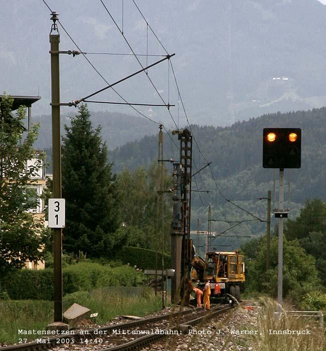 Eines Tages an der Mittenwaldbahn... I: Eines Tages vibriert die Gegend unter rhythmischen Schlgen, die sich keiner erklren kann, fast wie ein Herzschlag mit einem schweren Haupt- und einem leichten Nachschlag hrt es sich an. So macht man sich auf, um nach des Urwaldes Ursache zu suchen und findet die Bahn vor, die die Fundamente fr die neuen - mittlerweilen seit langem aufgerichteten - Betonmasten mit einer hydraulischen Ramme auf einem Zweiwegebagger in die unschuldige Httinger Erde hmmert. 27. Mai 2003