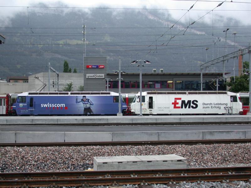 Ge 4/4 III 643 Vals  mit Ems Chemie Werbung und die Schesterlok 648 Susch  mit Swisscom Werbung sind aus St.Moritz eingetroffen und stehen hier am 11.07.2005 vor dem neuen Stellwerk Chur und dem vernebleten Calanda.