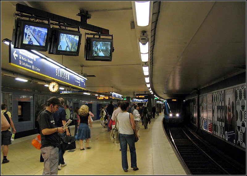 Grüne und Rote Linien, Station  Slussen  - 

Viergleisige Station im Richtungsbetrieb. Die grüne Strecke verläuft weiter in Richtung Süden, während die Roten Linie von hier im großen Bogen in in die südwestlichen Stadtteile fahren. Der weiterführende Tunnel durch Södermalm der Grünen Linie entstand schon in den dreißiger Jahren und wurde zunächst von Vorortstraßenbahnen betrieben. Am Platz des heutigen U-Bahnhofes lag die offene Endstation mit Wendeschleife. 

Auch nach Umstellung auf U-Bahnbetrieb am 1.10.1950 lag die Station Slussen noch zum großen Teil im Freien. Erst in den sechziger Jahren wurde sie vollständig abgedeckt. Am Nordende der Station gibt es Abgänge zum drunterliegenden Busbahnhof und zur Endstation der Saltjöbanan. In der Mitte führen Aufgänge zu einem oberirdischen Zugangsgebäude am Platz vor dem Stadmuséet. Am Südende liegen die Bahnsteig schon im Berg. Dort gibt einen weiteren Ausgang zu den höher liegenden Stadtgebieten an der Gotgatan. An diesen Ausgang soll in einigen Jahren eine neue Tunnelendhaltestelle der Saltsjö- und Tvärbanan angebunden werden. 

20.08.2007 (J)