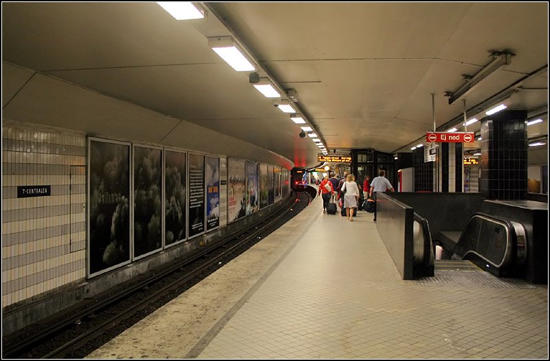 Grne und Rote Linien, Station  T-Centralen . Blick in die unter Bahnsteigebene der doppelstckigen Haltestelle. Hier fahren die Zge Ropsten und Mrby C (Rot, Richtung Nordosten) sowie die Bahnen der Grnen Linie in Richtung Sden. Der Treppenabgang rechts fhrt zu den Bahnsteigen der blauen Linien, die in groer Tieflage in den siebziger Jahren fertiggestellt wurden. Es treffen hier also alle Stockholmer U-Bahnlinien zusammen. Zudem besteht in T-Centralen bergang zum Hauptbahnhof (Stockholm C) und damit auch zu allen Pendeltg-Linien. Fr diese soll in den nchsten Jahren ein eigener Innenstadttunnel gebaut werden. Dabei entsteht hier in ca. 40 Meter Tiefe unter den U-Bahnhfen ein weiterer viergleisiger Tunnelbahnhof. Normalerweise sind die Bahnstieg nicht so leer, wie auf den Bildern, die an einem Sonntag-Vormittag entstanden. 19.8.2007 (Matthias)