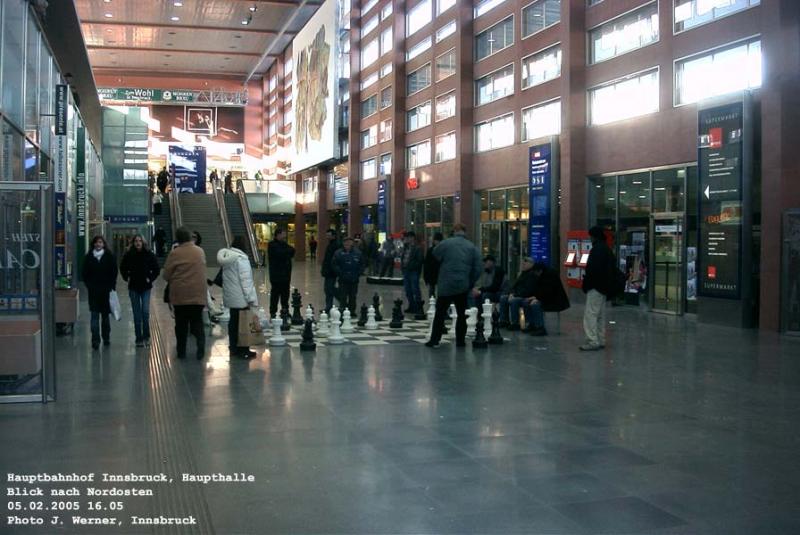 Haupthalle des Innsbrucker Bahnhofes, Blick nach Nordosten. Im Hintergrunde an der Wand eines der Weiler-Fresken, dem alten Bahnhof samt der Wand entnommen, entsprechend fixiert und am Mittenwaldbahnsteig zwischengelagert, dann restauriert und mit zwei Titan-N�geln wieder aufgeh�ngt erstrahlt es nun aufs Neue. Lustig finde ich auch die Idee, dieses Park-Schachbrett in der Halle anzubringen. 5. Februar 2005 kHds