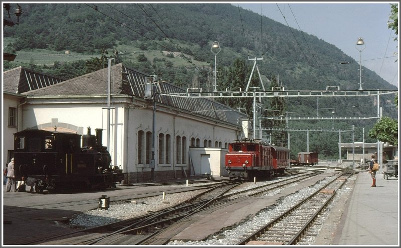 HGe 4/4 I 12 neben der Dampflok 7  Breithorn  vor dem Depot Visp. Man beachte auch die Wandermode, die sich zumindest in der Schweiz grundlegend verndert hat. (Archiv 06/77)